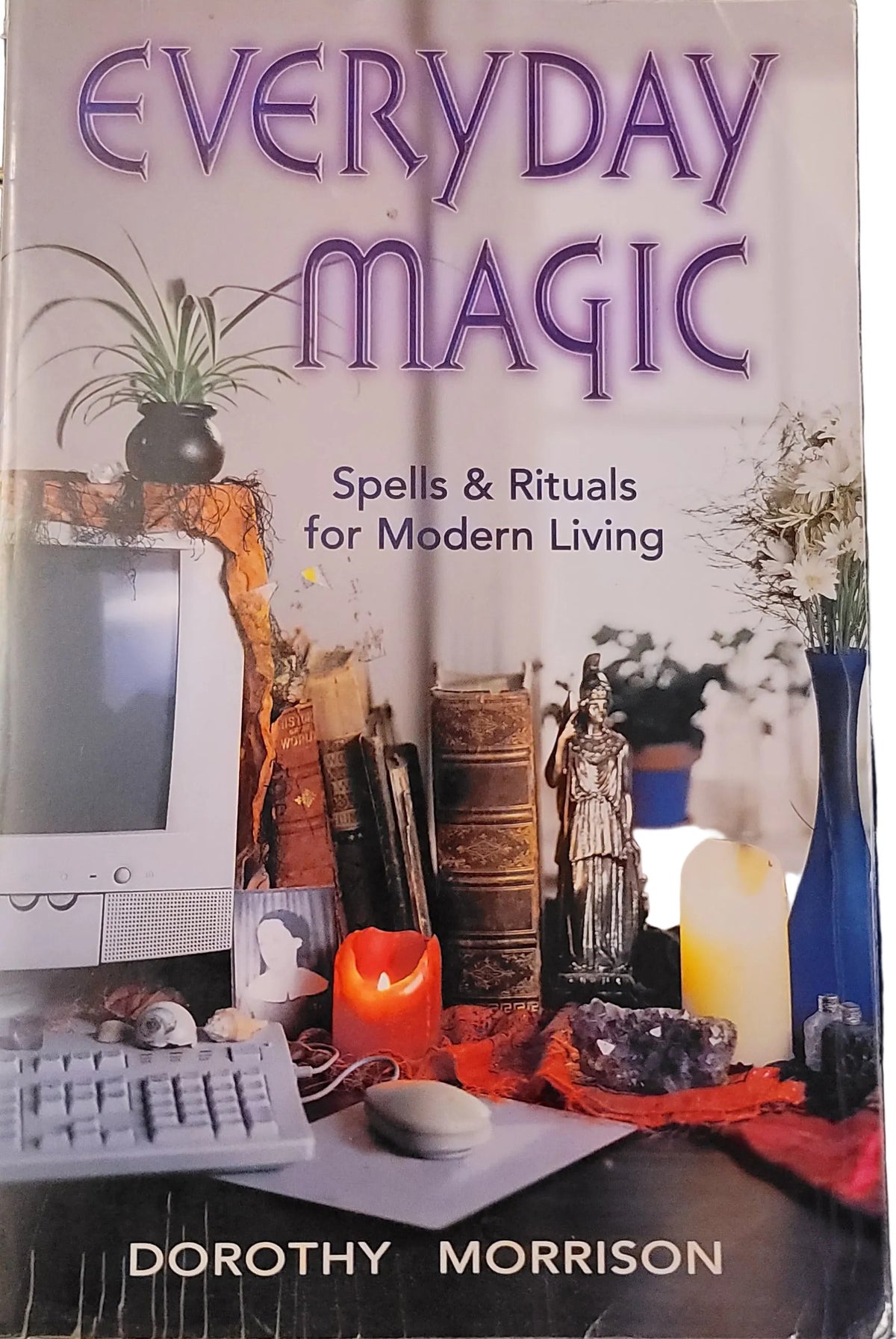 The front cover of the book 'Everyday Magic: Spells & Rituals for Modern Living' by Dorothy Morrison, featuring a collage of occult and mystical symbols, candles, crystals, and a computer monitor. The book is photographed flat on a dark, patterned surface.